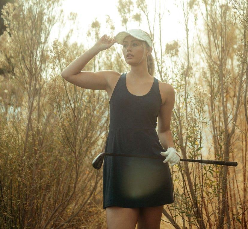 A woman holding a golf club wearing a KUHL Revivr dress
