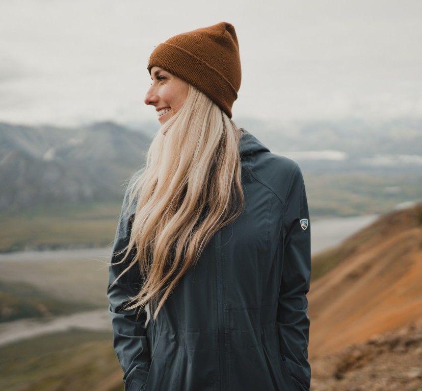A woman overlooking a lake wearing a KUHL Stretch Voyagr rain jacket
