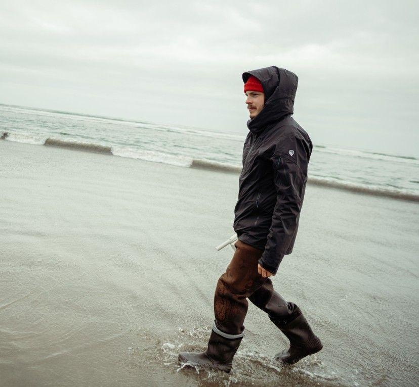 A man on a stormy beach wearing a KUHL rain jacket