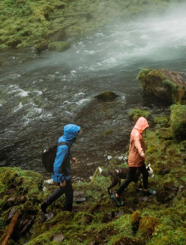 Two people visiting a waterfall wearing The One™ Shell jackets.