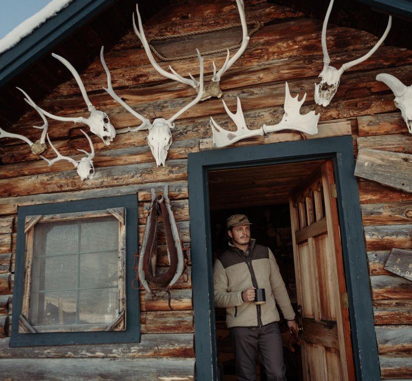 A man at the door of his wooden cabin wearing his Kühl Konfluence™ Fleece Jacket.
